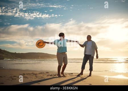 Love, couple and dancing on beach at sunset for romantic date, anniversary celebration or holiday. Sunshine, mature people or holding hands with Stock Photo