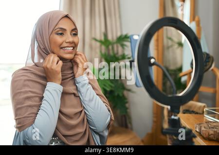 Cellphone, influencer and muslim woman in home for recording video on religious fashion. Light, phone and islamic female content creator with live Stock Photo