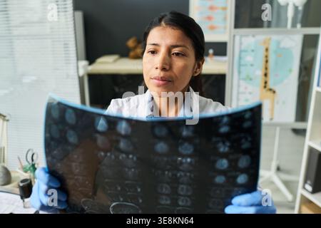 Female doctor examining brain scan film in clinic, assessing diagnosis and treatment planning. Ideal for healthcare, radiology, neurology, medical review concepts Stock Photo