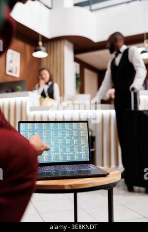 Manager shows notes on laptop, attending meeting with international business representative in hotel lounge area. Professional travelling for work, forging future partnership. Close up. Stock Photo