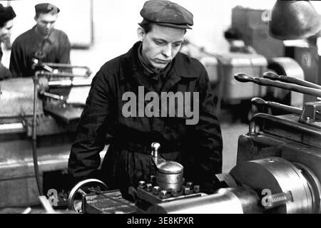 Sloviansk, 1980s, Armature and Insulator Plant (AIZ). This photograph captures the factory floor, featuring a young male worker in a cap leaning slightly forward as he continuously adjusts the heavy levers of a large industrial lathe machine during production. This archival image deeply highlights the technical processes, industrial machinery, and dedicated daily labor of Soviet workers driving the manufacturing sector. It preserves an essential historical record, offering a meaningful glimpse into life before the war in peaceful Donbas. Stock Photo