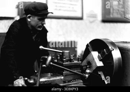 Sloviansk, 1980s, Armature and Insulator Plant (AIZ). This photograph captures the factory floor, featuring a young male worker in a cap standing attentively at his industrial lathe machine, observing the precision metal-cutting process taking place directly before him. This archival image deeply highlights the technical processes, industrial machinery, and dedicated daily labor of Soviet workers driving the manufacturing sector. It preserves an essential historical record, offering a meaningful glimpse into life before the war in peaceful Donbas. Stock Photo