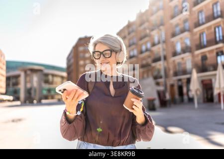 Mature woman enjoying coffee and music in city Stock Photo