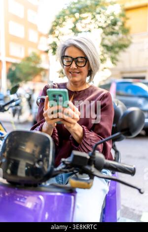 Woman using smartphone on scooter in city Stock Photo
