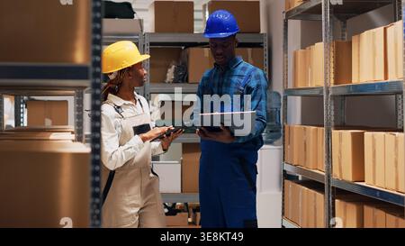 Two depot workers checking merchandise on shelves and planning order shipment or distribution, people looking at list of stock goods in warehouse. Products logistics and inventory. Stock Photo