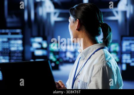 System administrator in data center uses laptop to prevent system overload during peak traffic periods. Overseeing manager in server farm ensuring enough network bandwidth for smooth operations Stock Photo