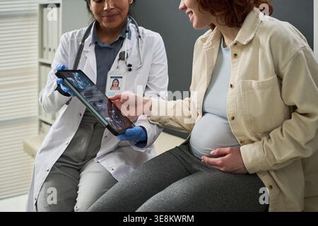 Female doctor showing ultrasound images on tablet to pregnant woman during prenatal consultation. Useful for maternity care, obstetrics, patient education marketing Stock Photo