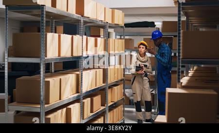Multiethnic team of workers scanning barcodes on boxes, looking at packages of goods in storage room depot. Two employees checking inventory to ship products in warehouse space. Stock Photo