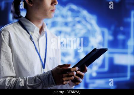 Admin using tablet in server farm to maintenance artificial intelligence neural networks simulating human thought processes in computerized model. High tech facility worker does checkup on AI systems Stock Photo