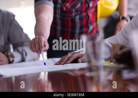 Business team reviewing architectural plans around conference table during construction project meeting Stock Photo