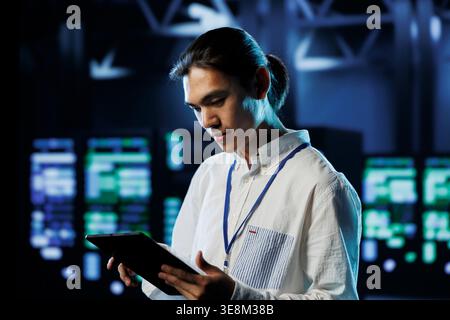 Knowledgeable developer between server hub clusters providing processing resources for businesses worldwide. Skilled employee fixes data center mainframes tasked with managing massive databases Stock Photo