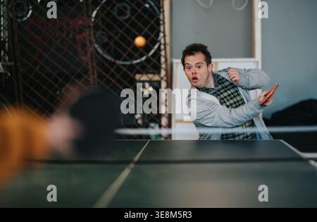 Young man with Down syndrome playing table tennis indoors with focused expression Stock Photo