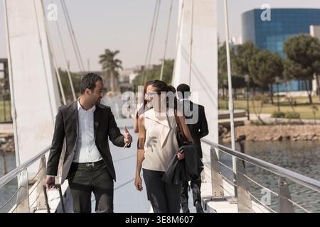 Business colleagues walking and talking on a modern bridge during a daytime outdoor commute Stock Photo
