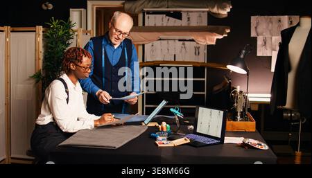 Trainee learning to craft clothing items, talking to experienced couturier about tailoring skills and needlework. Old tailor teaching student the handmade sewing process in atelier. Stock Photo