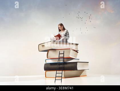 A girl child is sitting on pile of books isolated on free background. Stock Photo