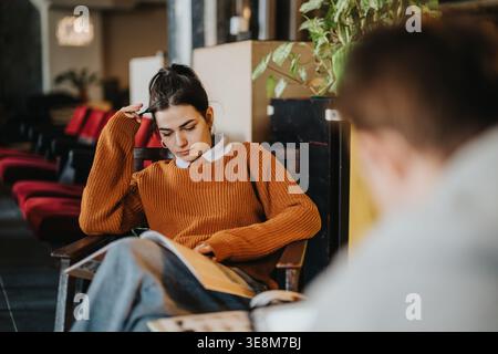 Female student reading and studying in a cozy lounge wearing an orange sweater Stock Photo