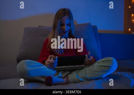 Excited laughing girl reacting to a video game on her console with blue and warm background lighting Stock Photo
