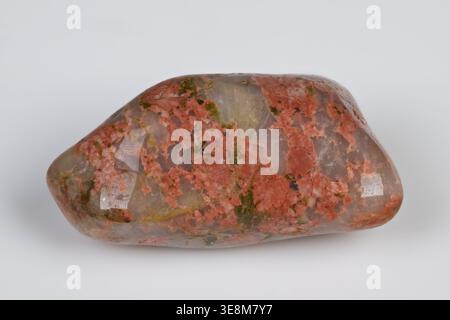 Polished unakite gemstone showcasing pink green mottling, elongated pebble with glossy finish, closeup studio shot on white background, visible epidot Stock Photo