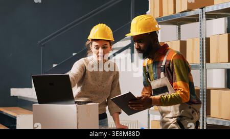 Delivery team checking packages in depot, working on supply chain for shipment and distribution. Man and woman reviewing logistics list on boxes, shipping merchandise. Handheld shot. Stock Photo