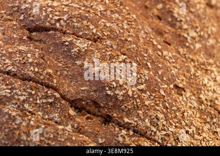 Macro top-down view of a sliced brown loaf with a flaky bran crust and diagonal slices of bread. Stock Photo