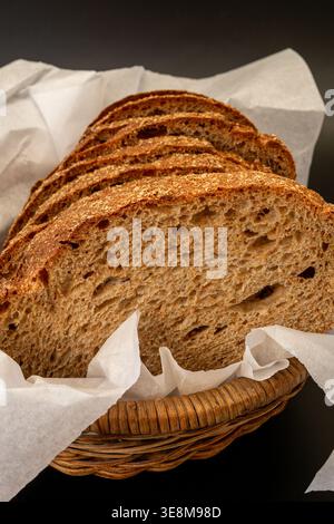Close-up view of sliced grain bread presented in a woven basket lined with white parchment paper on a minimalist black background. Stock Photo