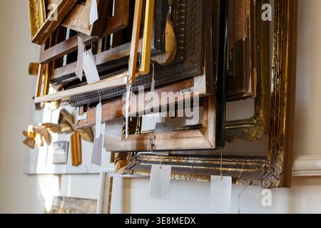 Old picture frames are stacked in a storage area. The collection shows different styles and sizes, waiting for new artwork. Stock Photo