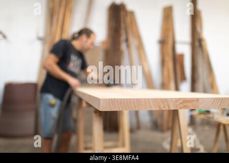 Carpenter sanding wood plank in workshop, crafting furniture Stock Photo