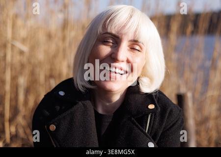 A close-up, detailed portrait of a young, beautiful woman laughing in the rays of the bright spring sun. Smiling blonde. Spring emotions. Stock Photo