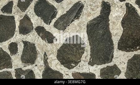 Close‑up of irregular stone mosaic pattern with dark rocks set in light mortar. Stock Photo