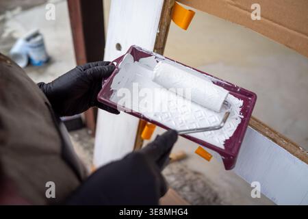 White paint in tray with roller, protective gloves and textured surface, closeup of prep stage for home Stock Photo