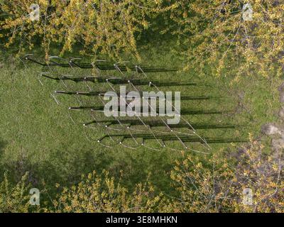 Aerial view of a metallic diamond grid casting stark shadows on the verdant lawn, framed by trees with yellow leaves, Almere, Flevoland, Netherlands. Stock Photo
