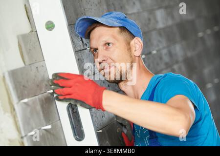 tiler controls level of installed decorating ceramic panel tile on wall in hall Stock Photo
