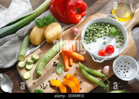 Assorted seasonal vegetables with vintage kitchen utensils on wooden cutting board. High-angle shot features sliced carrots pumpkin zucchini and Stock Photo