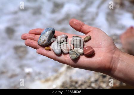 Albanian Riviera view in summer. Borsh beach in Vlore County, Albania. Hand holding colorful souvenir beach pebbles. Stock Photo