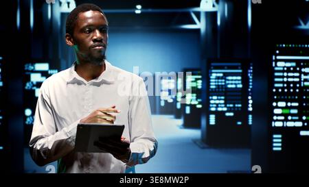 IT administrator in hardware room housing server rackmounts, storage devices and networking units providing vast amounts of computing resources. Supervisor doing equipment maintenance Stock Photo