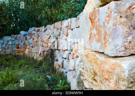A rustic, hand-built stone wall curves through a natural landscape, showcasing textured rocks and surrounding vegetation Stock Photo