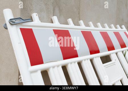 A temporary white plastic barrier with alternating red and white diagonal stripes, used for traffic control and safety on construction sites Stock Photo