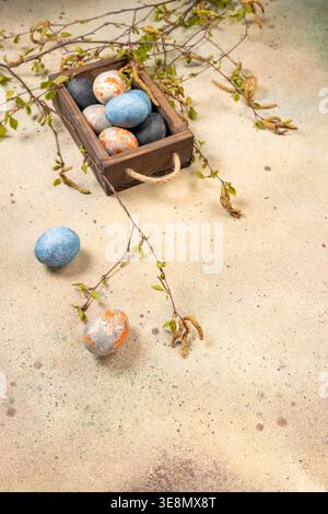 Colorful marbled easter eggs resting in a rustic wooden crate, surrounded by fresh birch branches with budding leaves and catkins, symbolizing spring Stock Photo