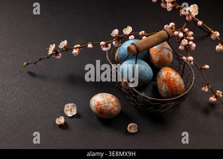 Colorful marbled easter eggs in a vintage wire basket with blossoming spring branches, symbolizing renewal, new beginnings, and holiday celebration on Stock Photo