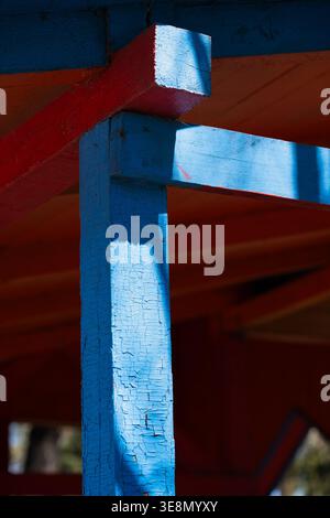 Close-up of blue and red painted wooden beams with peeling texture. Minimalist architectural detail with vibrant colors and weathered wood texture. Stock Photo