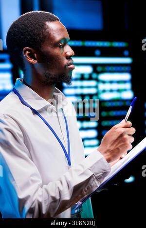 Expert conducting diagnostic tests on server racks to identify and rectify issues with data center equipment. Admin meticulously reviewing maintenance checklist, closely monitoring critical systems Stock Photo