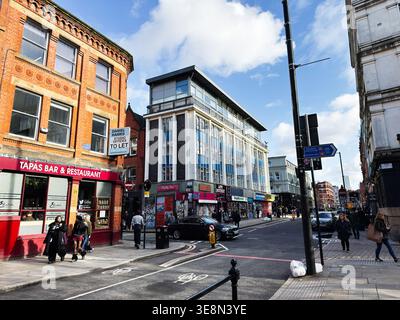 Manchester, UK - February 22, 2026: Pedestrians walk past shops and a tapas bar on a bright urban street in Manchester, UK. Stock Photo