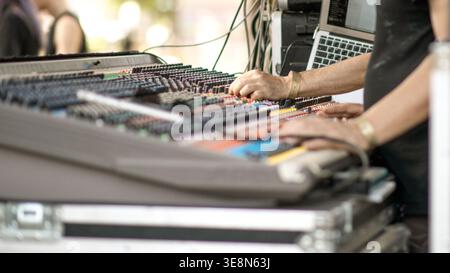 Hands adjust controls on an audio mixing console connected to equipment in an outdoor setup. Stock Photo