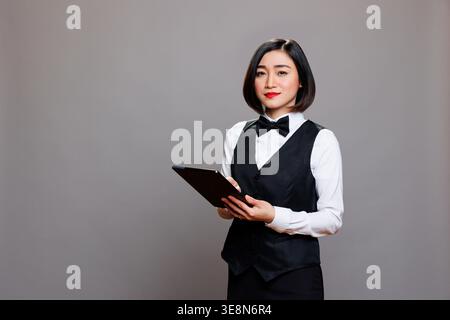Smiling confident asian waitress wearing professional uniform, holding digital tablet and looking at camera. Young attractive hospitality industry receptionist using portable gadget portrait Stock Photo