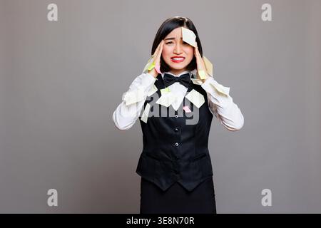 Frustrated asian woman receptionist with sticky notes on face multitasking, panicking and looking at camera. Stressed exhausted busy restaurant waitress overloaded with work portrait Stock Photo
