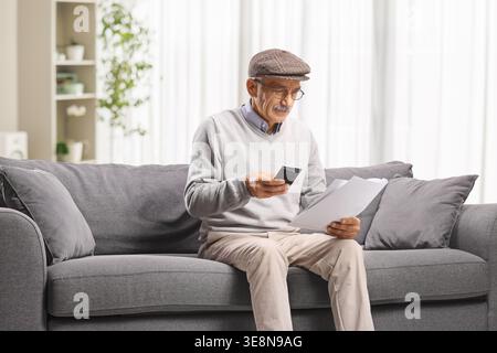 Senior man calculating bills at home seated on a sofa Stock Photo