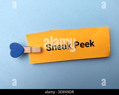 A conceptual high angle studio shot featuring an orange paper slip with the words Sneak Peek. Stock Photo