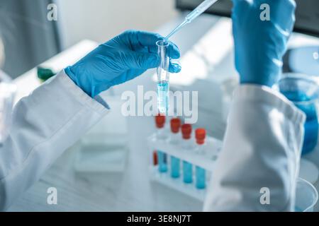 Closeup of hands in blue gloves handling laboratory glassware and pipette with blue solution, focusing on scientific research. Modern lab setting highlights innovation and technology in chemistry Stock Photo