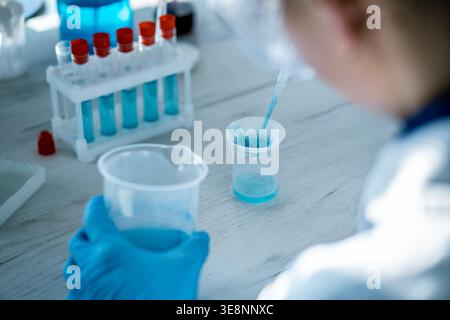 Close up of laboratory technician conducting chemical experiment with blue solution using pipette and beaker. Innovative scientific research and advanced laboratory testing in progress Stock Photo