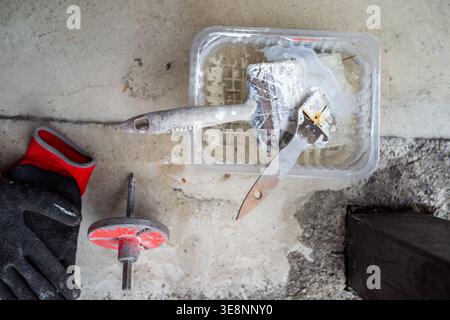Plastering tools on concrete floor, closeup showing plaster tray, putty knife, roller and sanding disc next Stock Photo